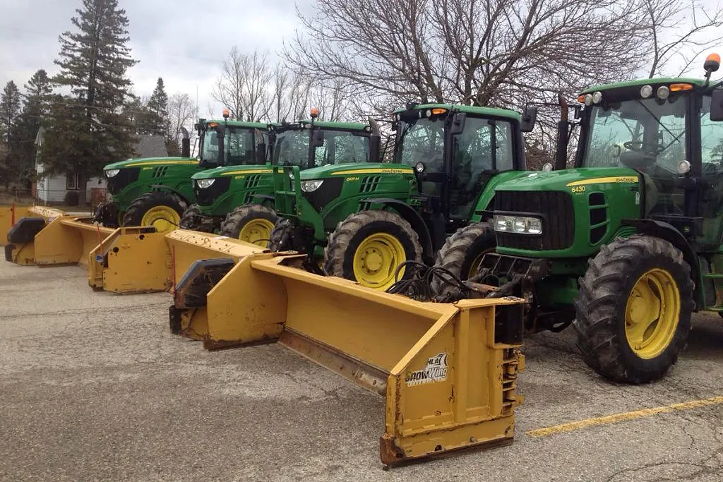 Four Acres tractors with yellow snow pushers lined up in a lot
